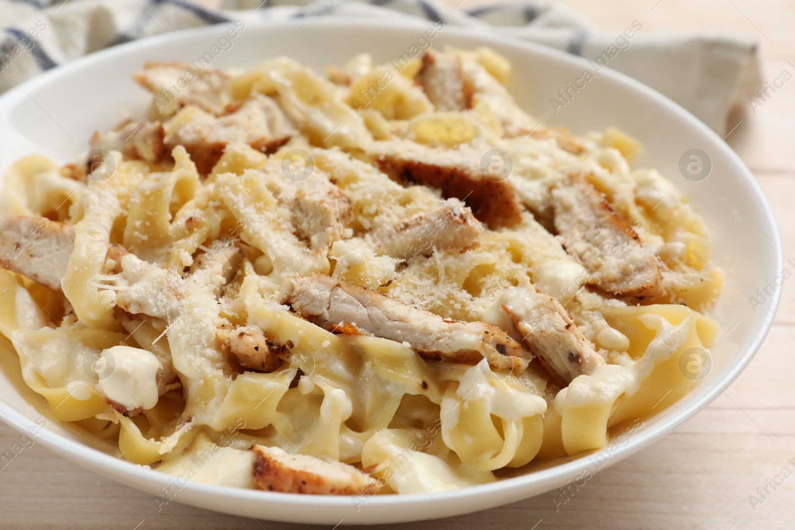 Photo of Tasty Alfredo pasta with chicken on light wooden table, closeup