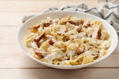 Photo of Tasty Alfredo pasta with chicken on light wooden table, closeup