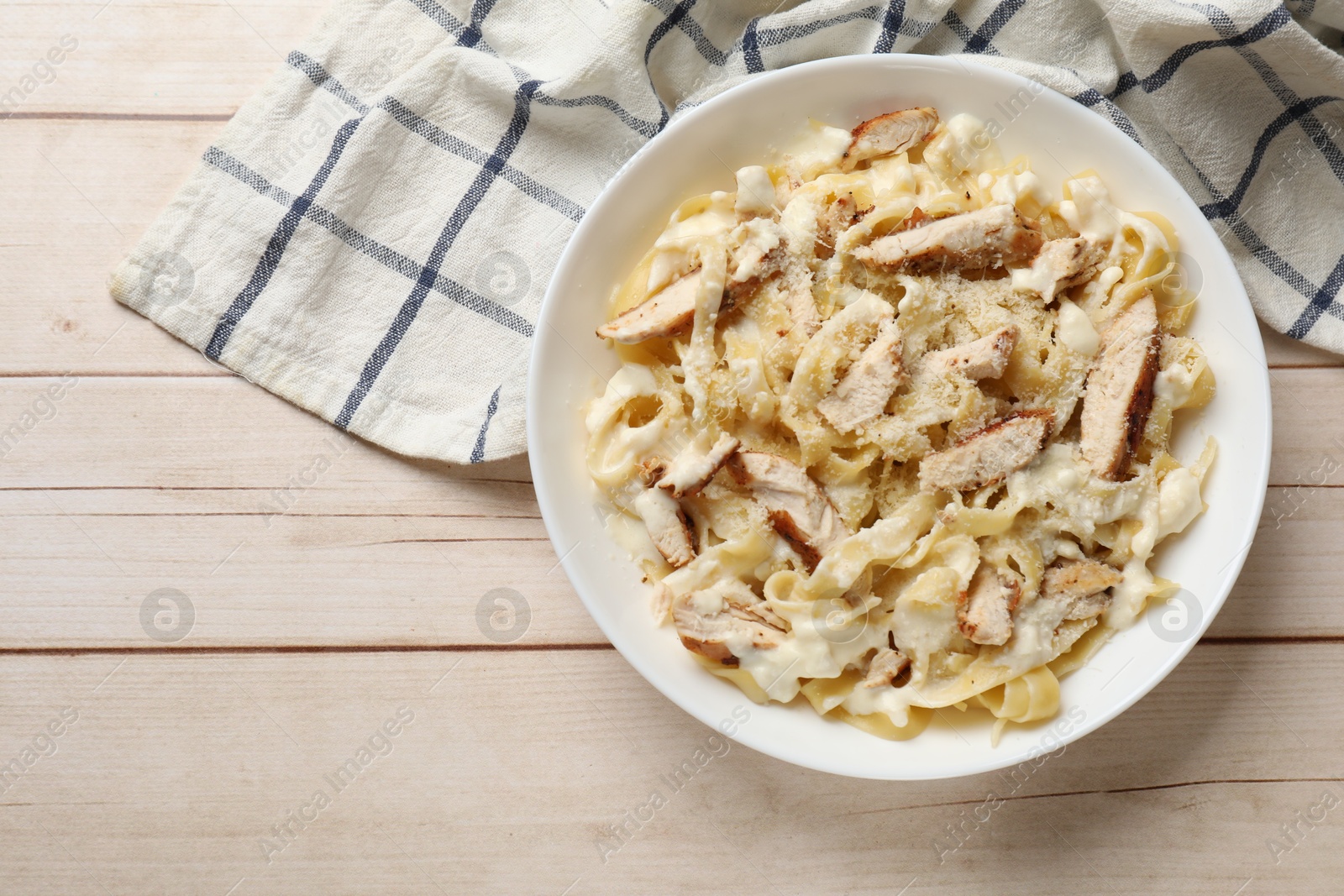 Photo of Tasty Alfredo pasta with chicken on light wooden table, top view. Space for text