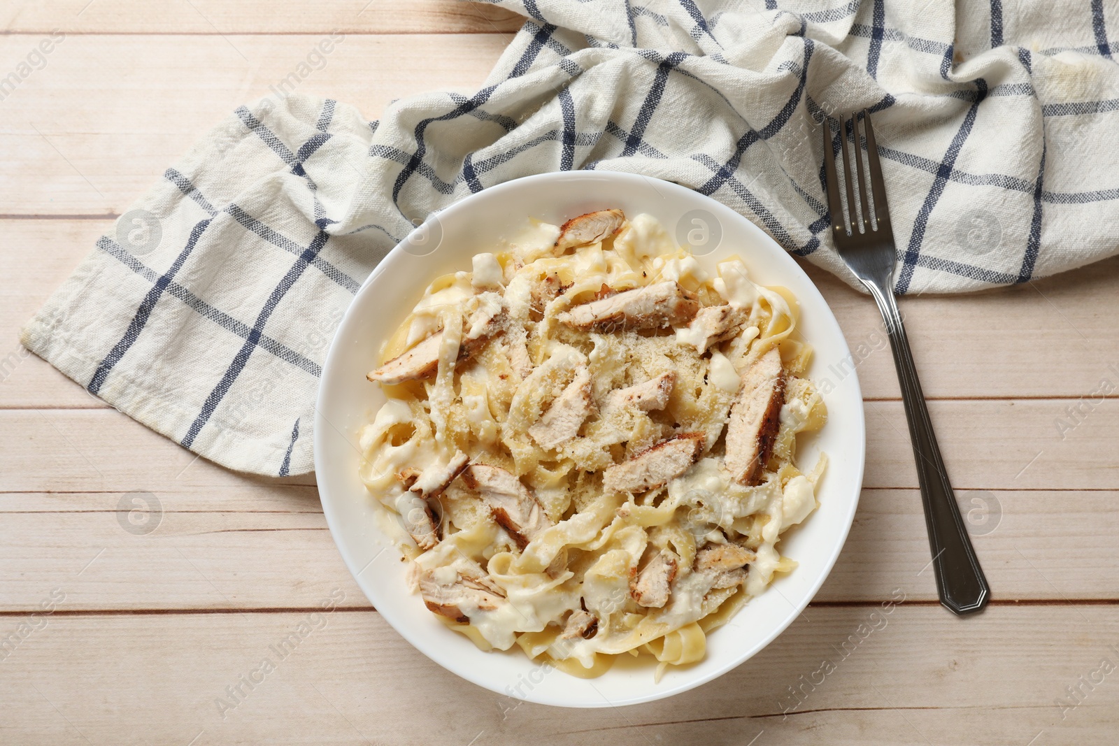 Photo of Tasty Alfredo pasta with chicken served on light wooden table, top view