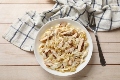 Photo of Tasty Alfredo pasta with chicken served on light wooden table, top view