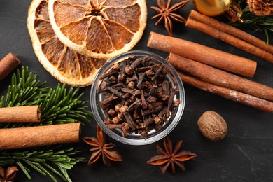 Photo of Different aromatic spices and fir tree branches on black table, flat lay. Christmas season