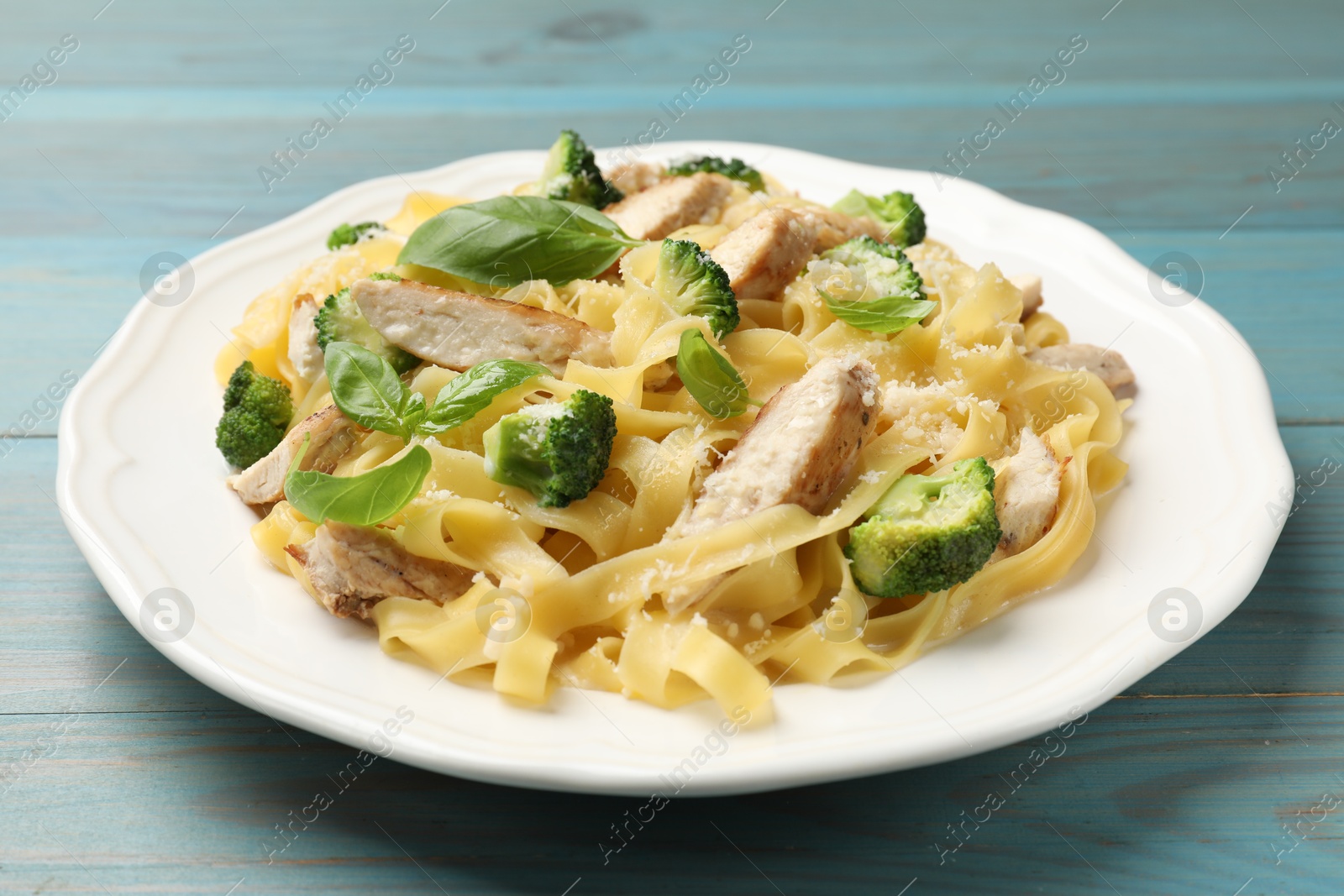 Photo of Delicious pasta Alfredo with chicken, cheese, broccoli and basil on light blue wooden table, closeup