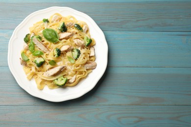 Photo of Delicious pasta Alfredo with chicken, cheese, broccoli and basil on light blue wooden table, top view. Space for text