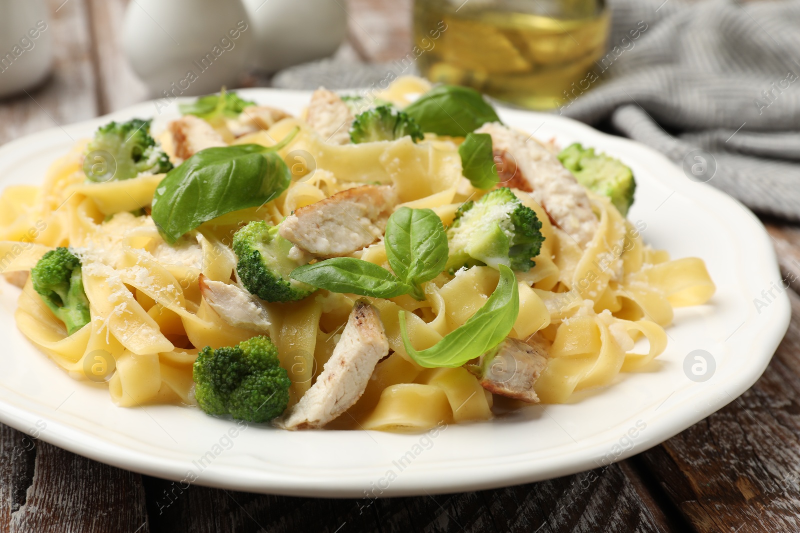 Photo of Delicious pasta Alfredo with chicken, cheese, broccoli and basil on wooden table, closeup