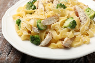 Photo of Delicious pasta Alfredo with chicken, cheese and broccoli on wooden table, closeup