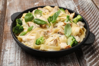 Photo of Delicious pasta Alfredo with chicken, cheese, creamy sauce, broccoli and basil on wooden table, closeup