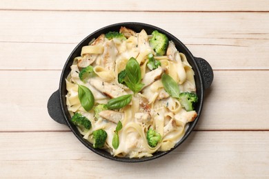 Photo of Delicious pasta Alfredo with chicken, cheese, creamy sauce, broccoli and basil on wooden table, top view