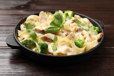 Photo of Delicious pasta Alfredo with chicken, cheese, creamy sauce, broccoli and basil on wooden table, closeup