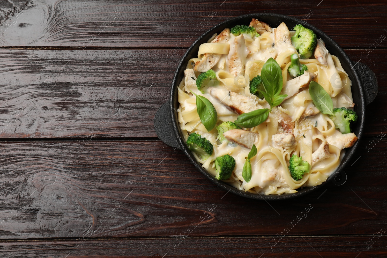 Photo of Delicious pasta Alfredo with chicken, cheese, creamy sauce, broccoli and basil on wooden table, top view. Space for text