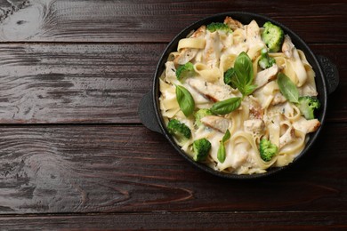 Photo of Delicious pasta Alfredo with chicken, cheese, creamy sauce, broccoli and basil on wooden table, top view. Space for text