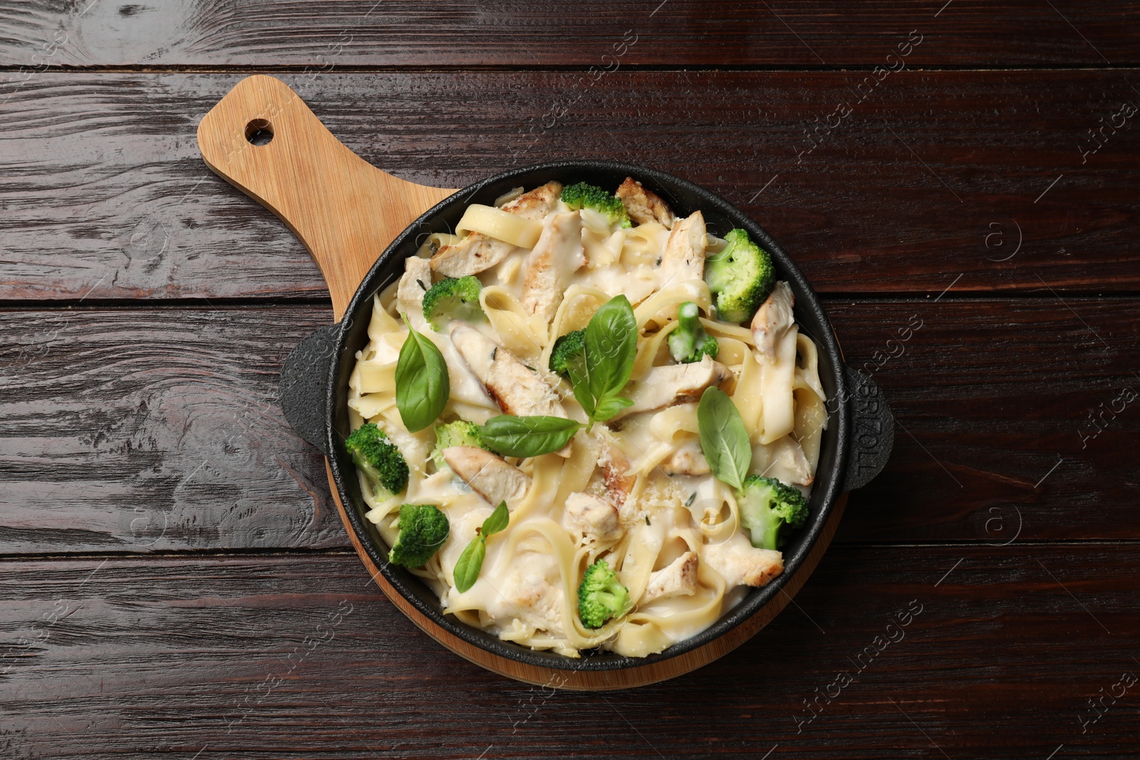 Photo of Delicious pasta Alfredo with chicken, cheese, creamy sauce, broccoli and basil on wooden table, top view