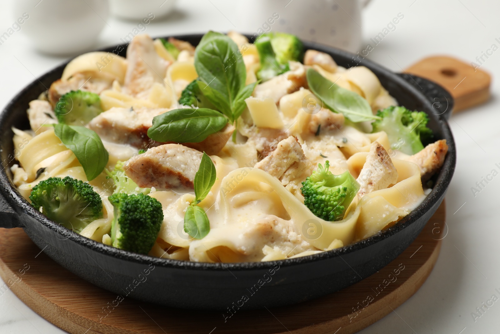 Photo of Delicious pasta Alfredo with chicken, cheese, creamy sauce, broccoli and basil on white table, closeup