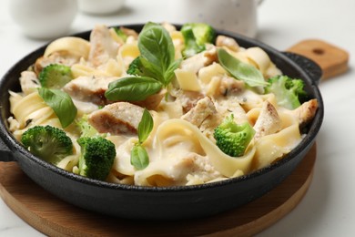 Photo of Delicious pasta Alfredo with chicken, cheese, creamy sauce, broccoli and basil on white table, closeup