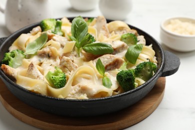 Photo of Delicious pasta Alfredo with chicken, cheese, creamy sauce, broccoli and basil on white table, closeup