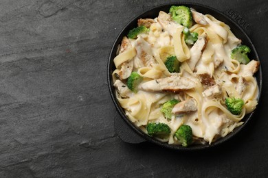 Photo of Delicious pasta Alfredo with chicken, cheese, creamy sauce and broccoli on black table, top view. Space for text