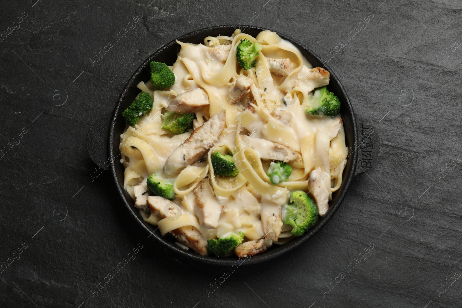 Photo of Delicious pasta Alfredo with chicken, cheese, creamy sauce and broccoli on black table, top view