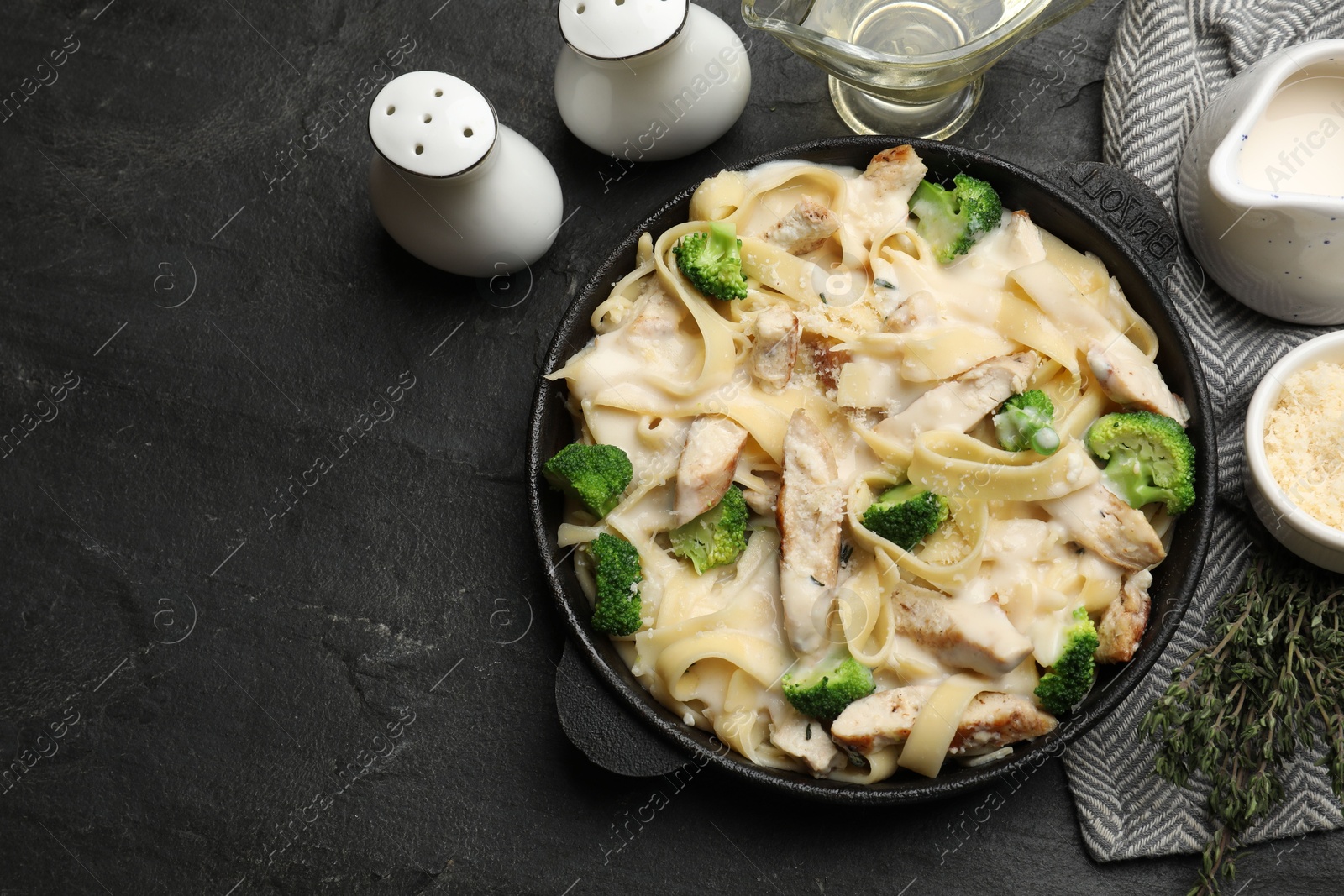 Photo of Delicious pasta Alfredo with chicken served on black table, flat lay. Space for text