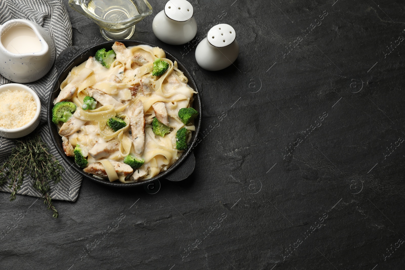 Photo of Delicious pasta Alfredo with chicken served on black table, flat lay. Space for text