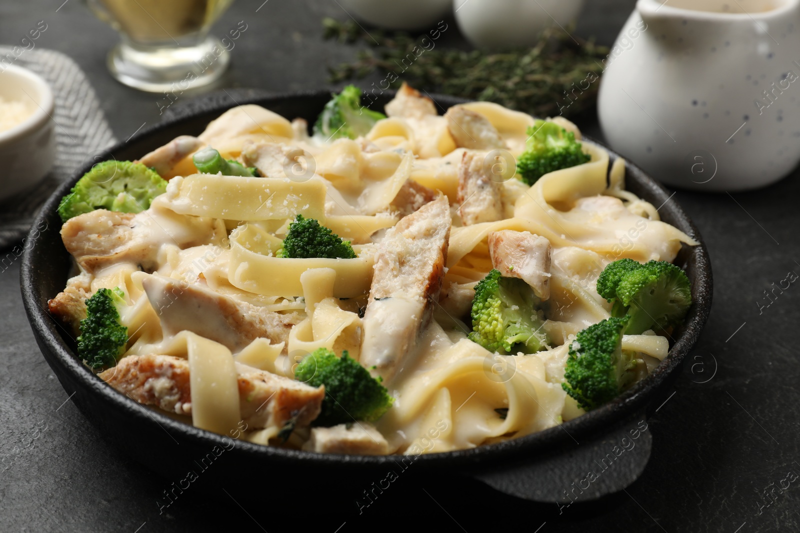 Photo of Delicious pasta Alfredo with chicken, cheese, creamy sauce and broccoli on black table, closeup