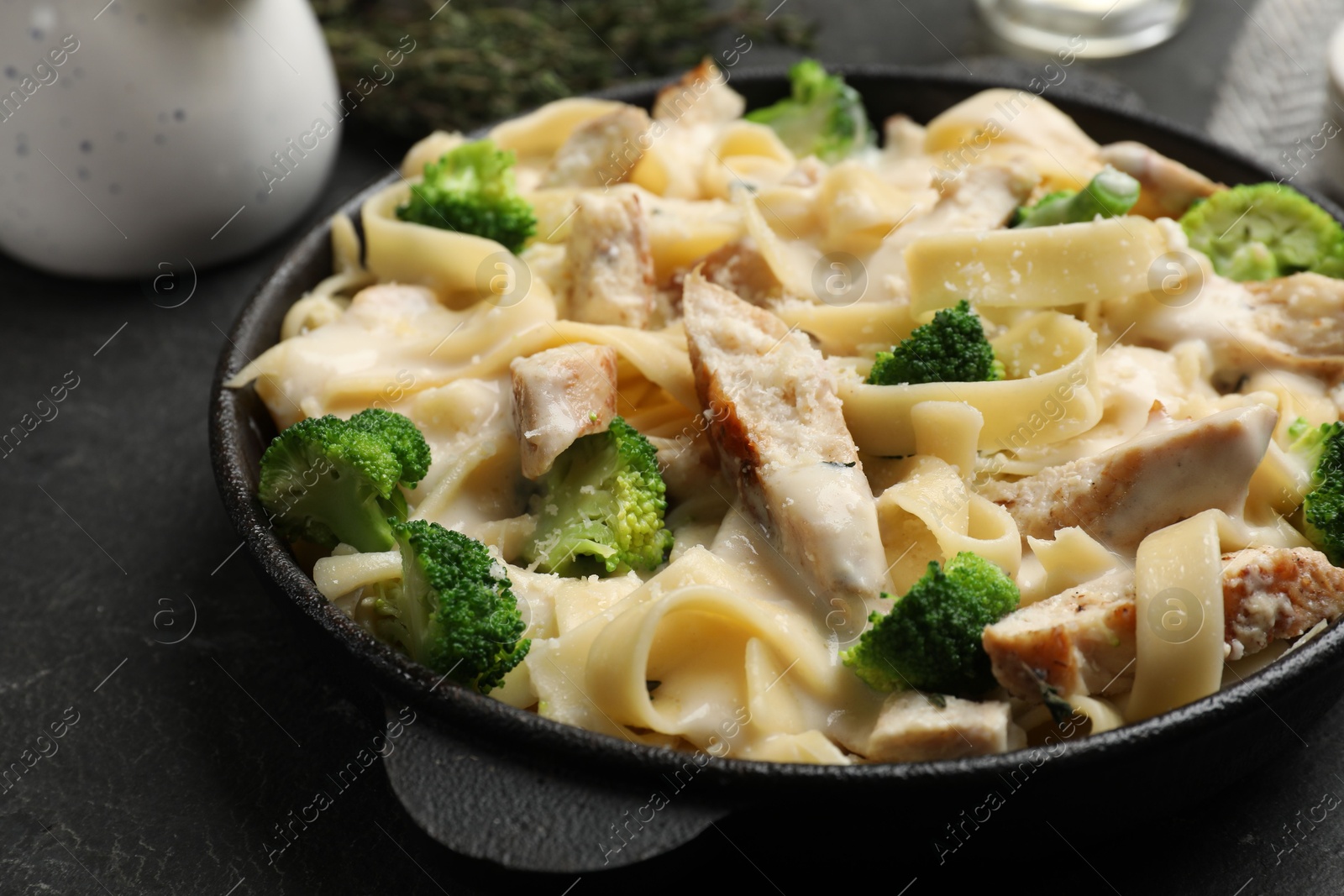 Photo of Delicious pasta Alfredo with chicken, cheese, creamy sauce and broccoli on black table, closeup