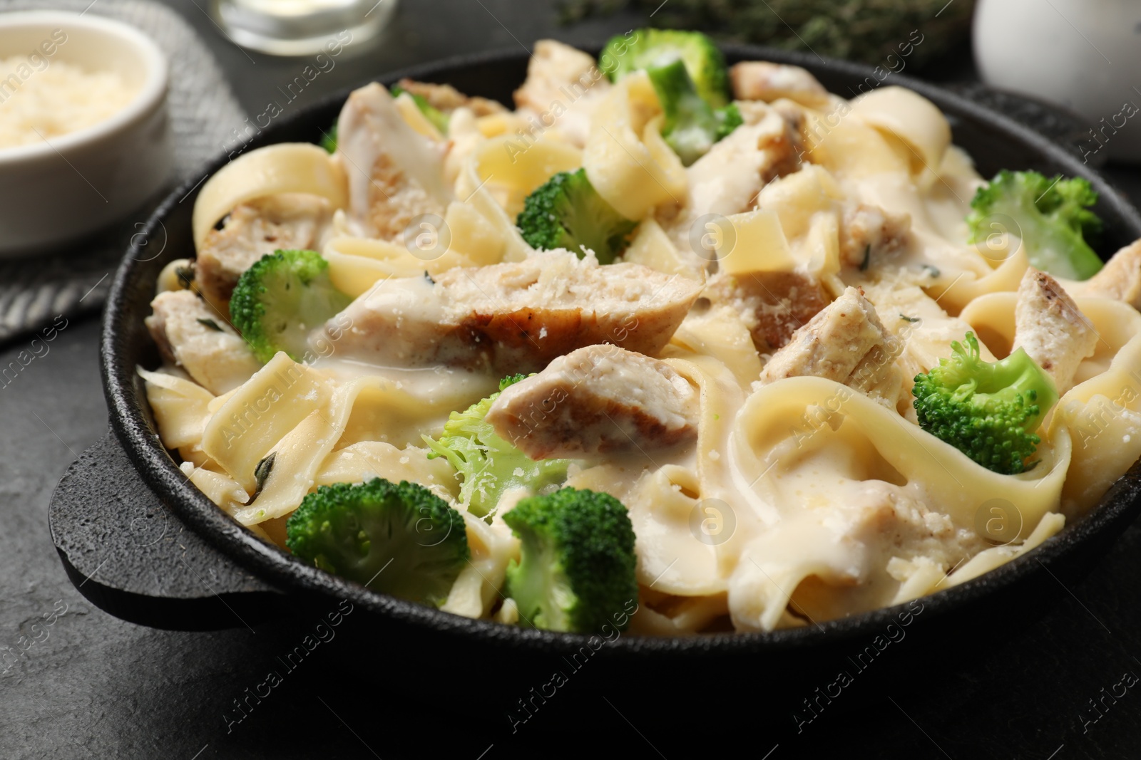 Photo of Delicious pasta Alfredo with chicken, cheese, creamy sauce and broccoli on black table, closeup