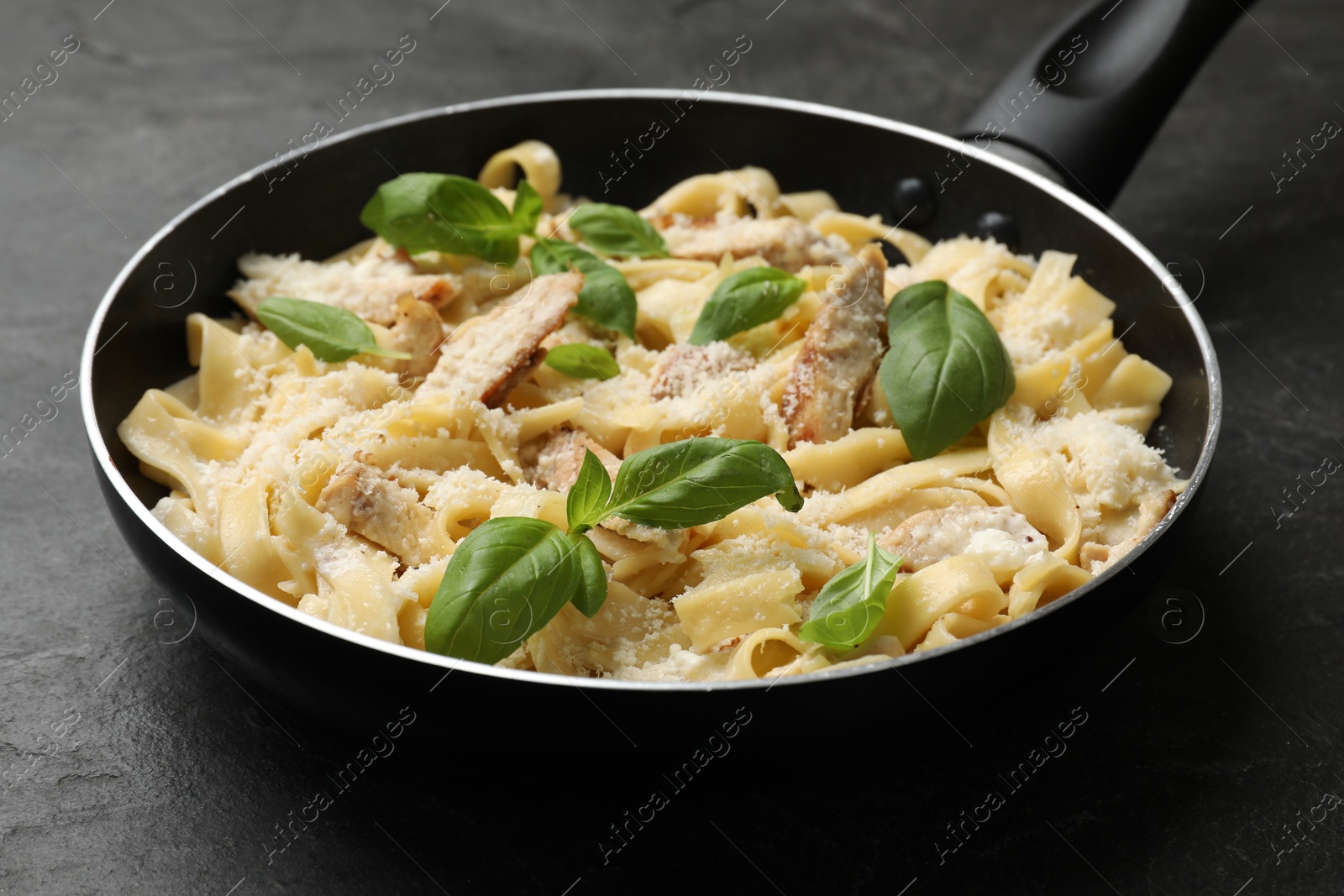 Photo of Delicious pasta Alfredo with chicken, cheese and basil in frying pan on black table, closeup