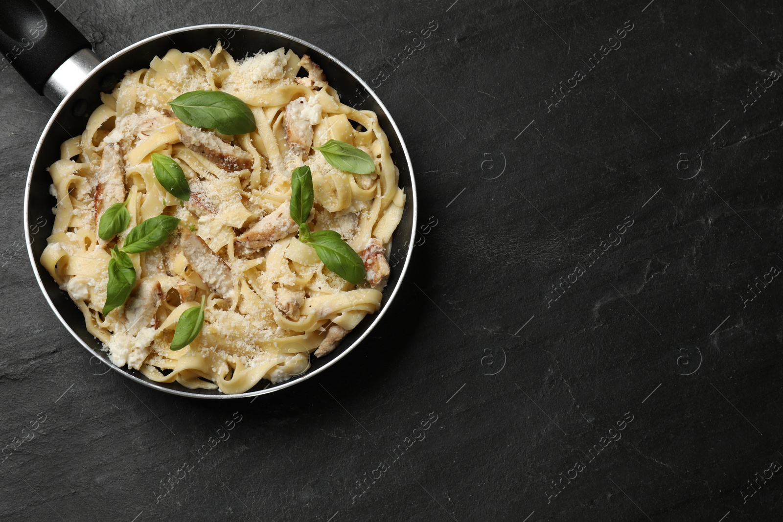 Photo of Delicious pasta Alfredo with chicken, cheese and basil in frying pan on black table, top view. Space for text