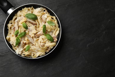 Photo of Delicious pasta Alfredo with chicken, cheese and basil in frying pan on black table, top view. Space for text