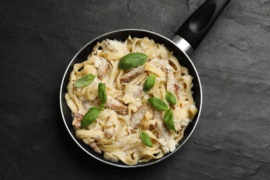 Photo of Delicious pasta Alfredo with chicken, cheese and basil in frying pan on black table, top view