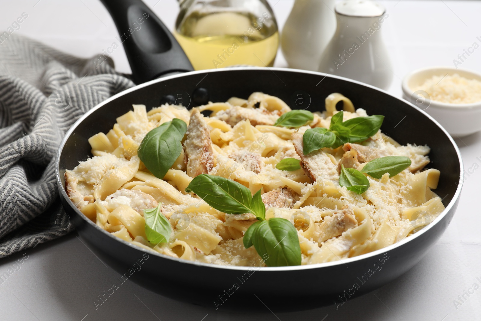 Photo of Delicious pasta Alfredo with chicken, cheese and basil in frying pan on white table, closeup