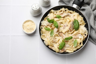 Photo of Delicious pasta Alfredo with chicken, cheese and basil on white tiled table, flat lay