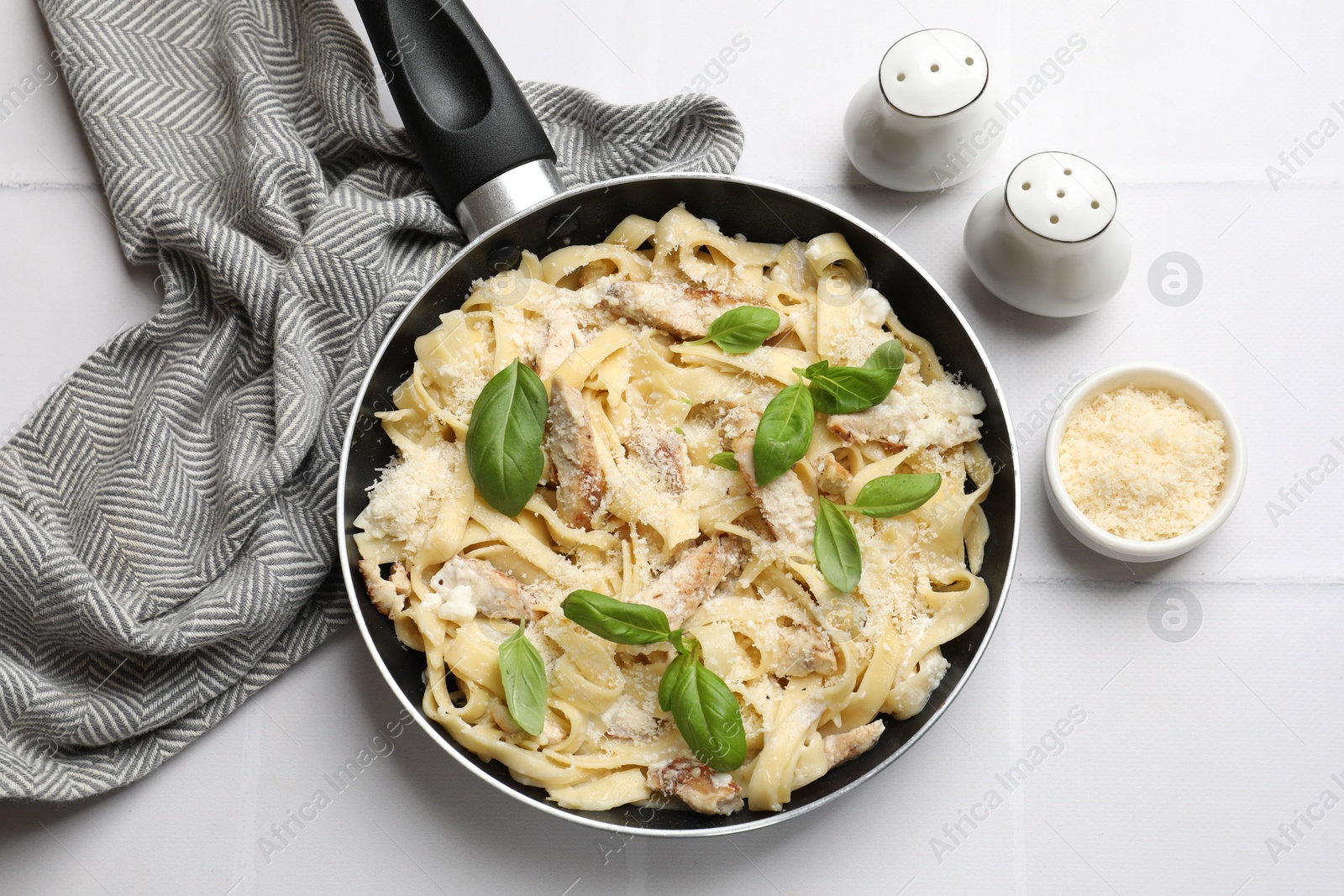 Photo of Delicious pasta Alfredo with chicken, cheese and basil on white tiled table, flat lay