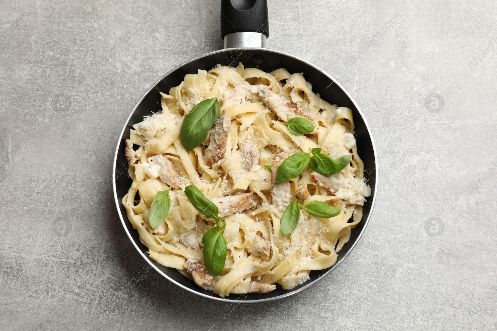 Photo of Delicious pasta Alfredo with chicken, cheese and basil in frying pan on grey table, top view