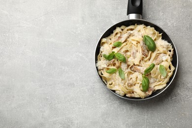 Photo of Delicious pasta Alfredo with chicken, cheese and basil in frying pan on grey table, top view. Space for text