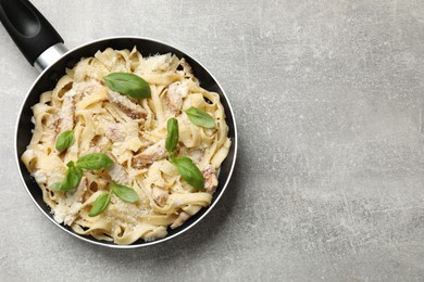 Photo of Delicious pasta Alfredo with chicken, cheese and basil in frying pan on grey table, top view. Space for text