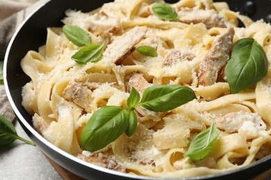 Photo of Delicious pasta Alfredo with chicken, cheese and basil in frying pan on table, closeup