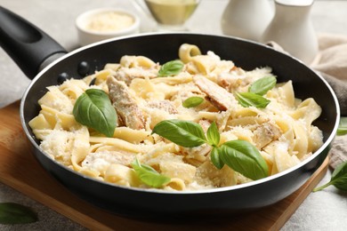 Photo of Delicious pasta Alfredo with chicken, cheese and basil in frying pan on table, closeup