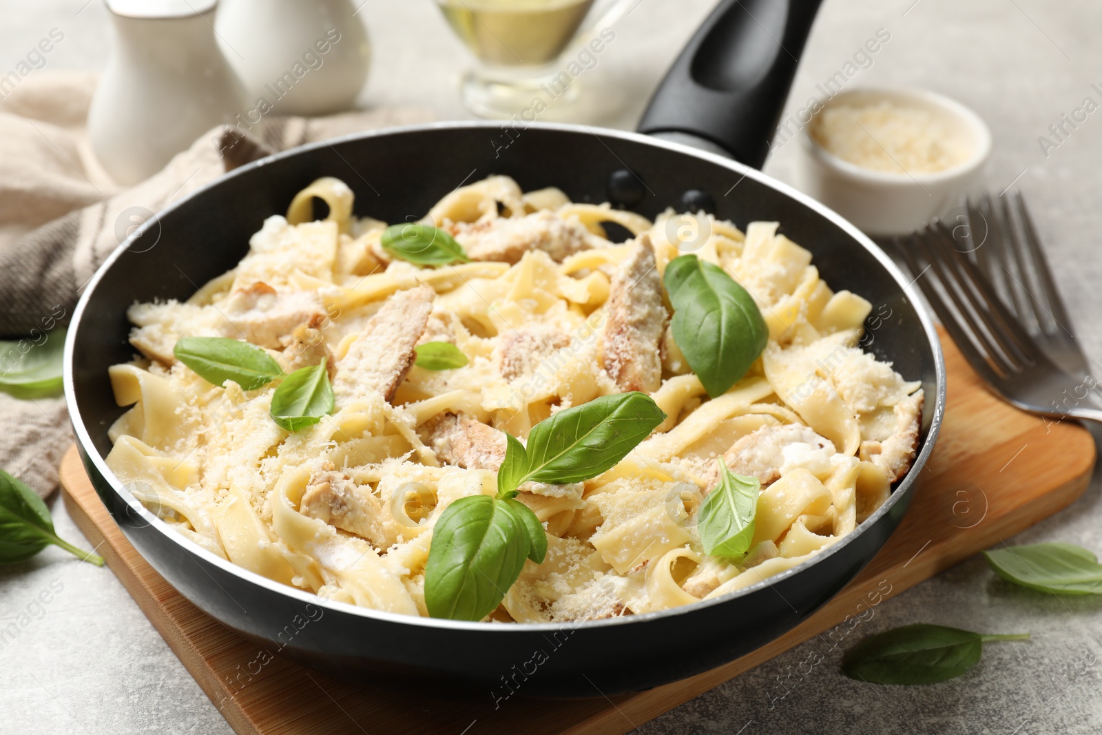 Photo of Delicious pasta Alfredo with chicken, cheese and basil in frying pan on grey table, closeup