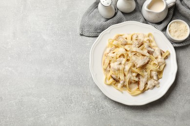 Photo of Tasty Alfredo pasta with chicken, cheese and creamy sauce on gray textured table, flat lay. Space for text