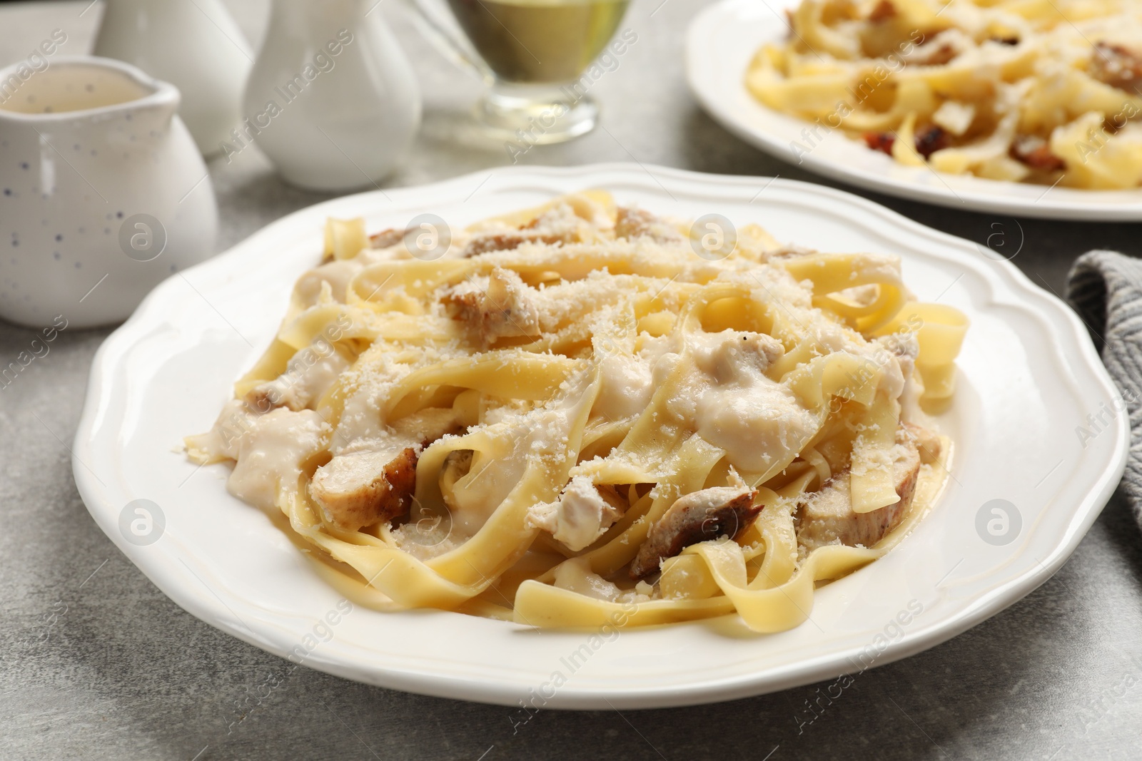 Photo of Tasty Alfredo pasta with chicken on gray textured table, closeup