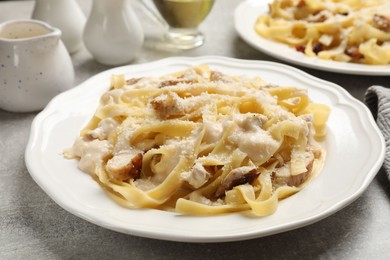 Photo of Tasty Alfredo pasta with chicken on gray textured table, closeup