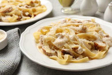 Photo of Tasty Alfredo pasta with chicken on gray textured table, closeup