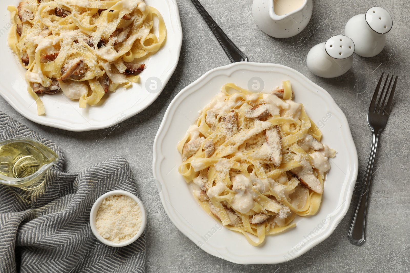 Photo of Tasty Alfredo pasta with chicken served on gray textured table, flat lay