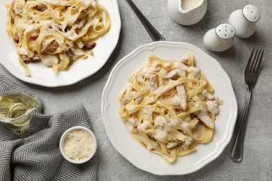 Photo of Tasty Alfredo pasta with chicken served on gray textured table, flat lay