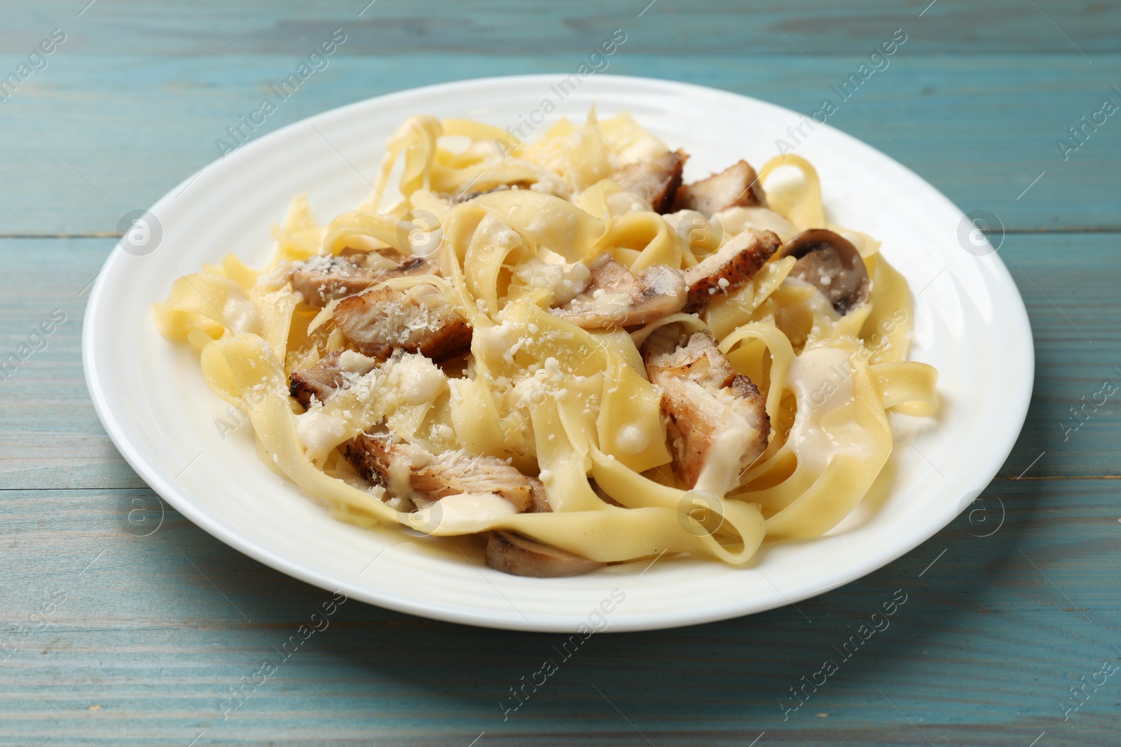 Photo of Tasty Alfredo pasta with chicken and mushrooms on light blue wooden table, closeup