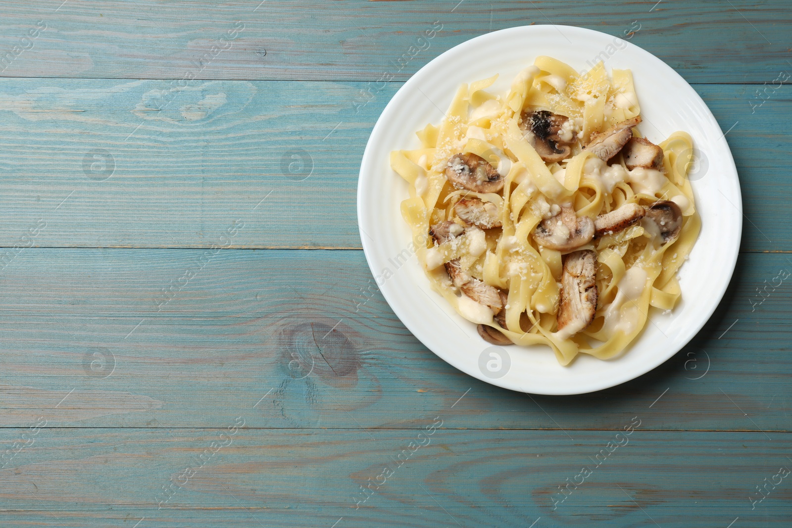 Photo of Tasty Alfredo pasta with chicken and mushrooms on light blue wooden table, top view. Space for text