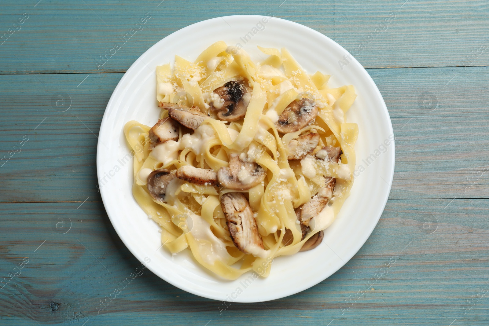 Photo of Tasty Alfredo pasta with chicken and mushrooms on light blue wooden table, top view