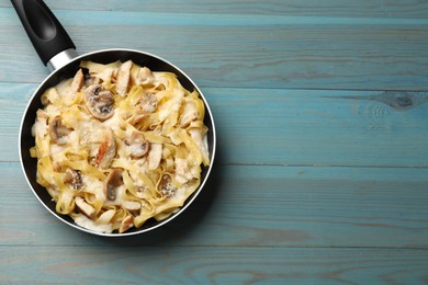 Photo of Tasty Alfredo pasta with chicken and mushrooms in frying pan on light blue wooden table, top view. Space for text