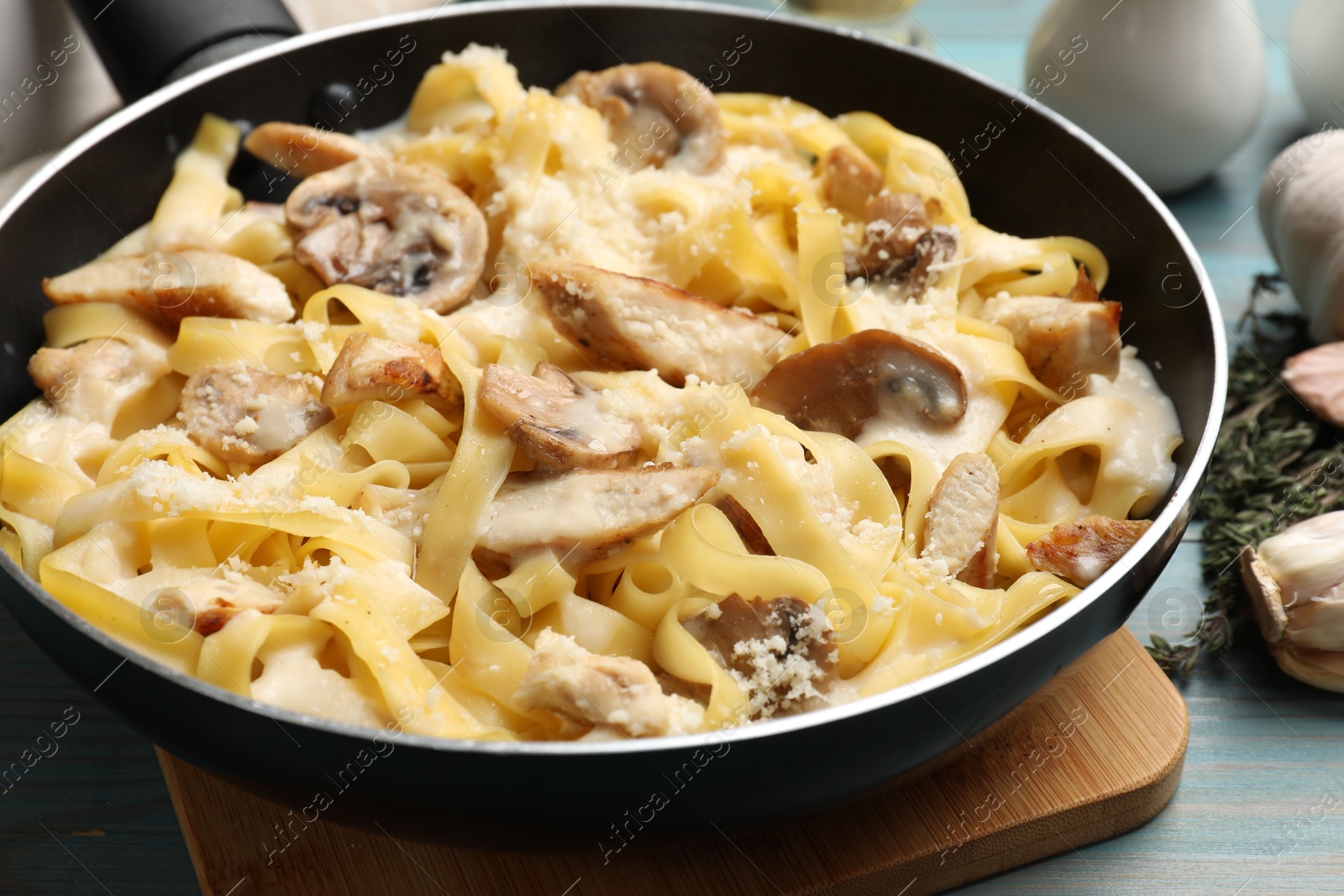 Photo of Tasty Alfredo pasta with chicken and mushrooms in frying pan on light blue wooden table, closeup